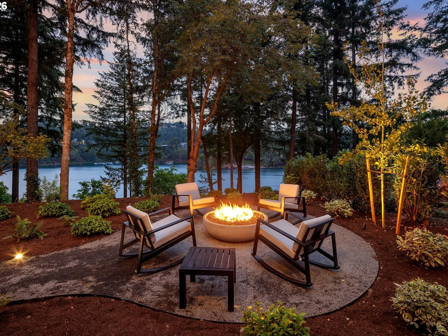 Lakeside fire pit area at dusk with stone pavers and mature trees near the water