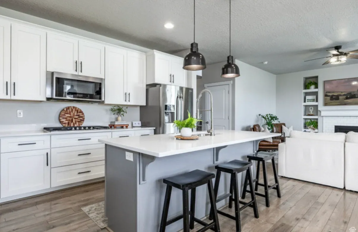 Open-concept kitchen with white shaker cabinets, grey island, and stainless steel appliances