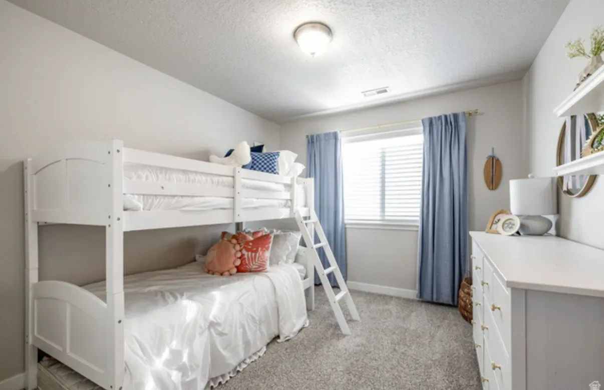 Secondary bedroom with white bunk bed, dresser, and circular mirror
