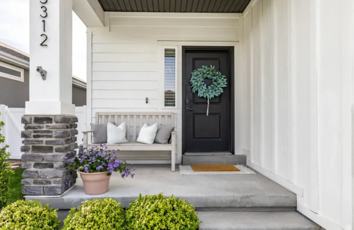 Front porch entryway with wooden bench, potted plant, and wreath on the black front door