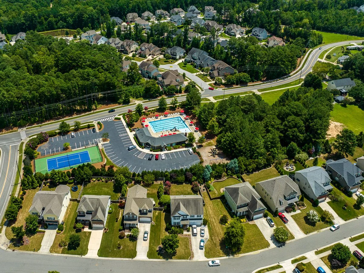 Aerial view of a neighborhood amenity center with a clubhouse, pool, and tennis courts