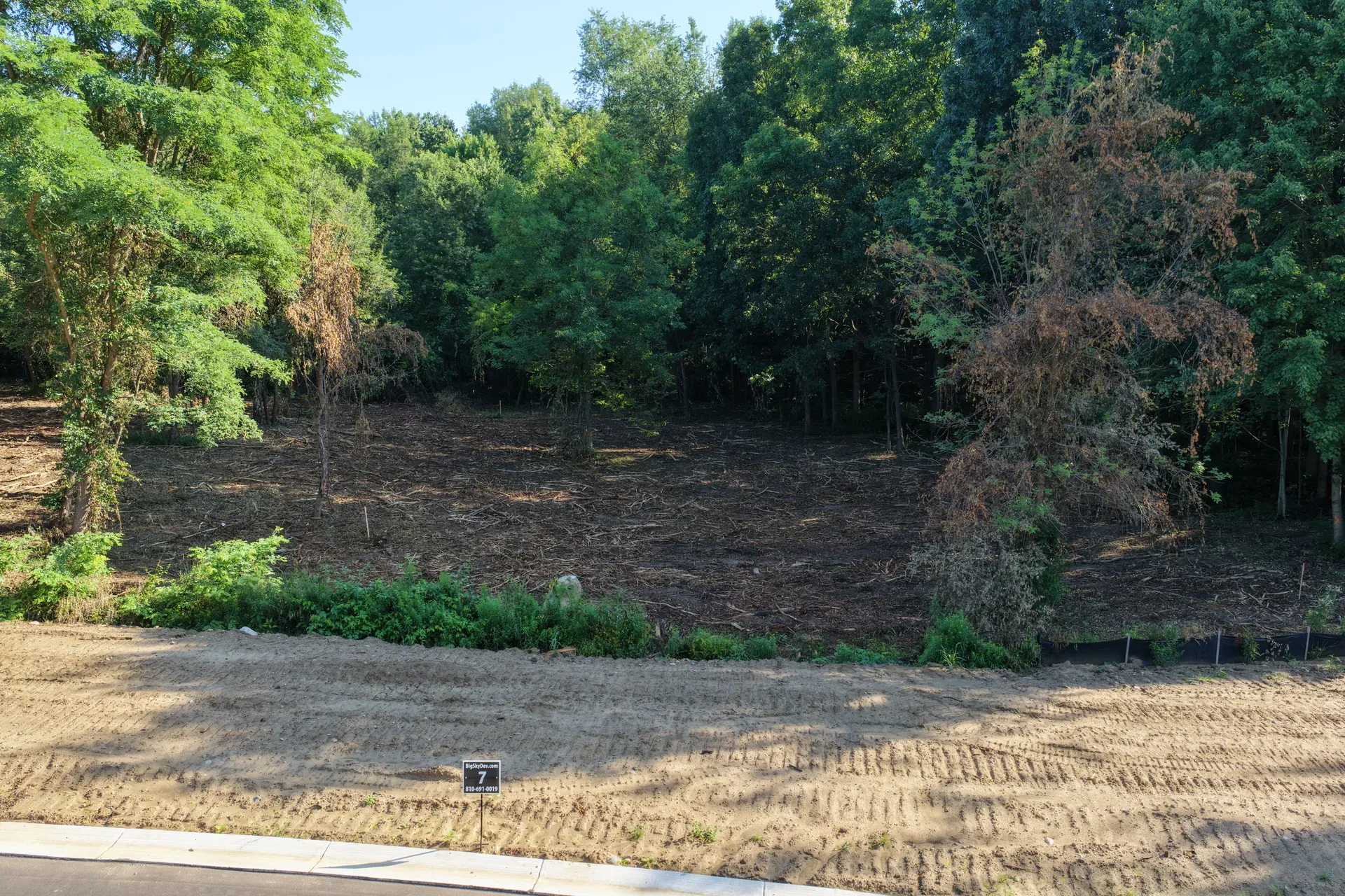 Drone aerial of an undeveloped residential lot at Oaks of Tyrone with wooded tree line and open building envelope in Tyrone Township Michigan