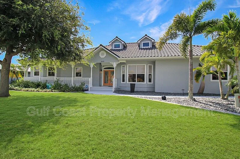 3415 Tripoli Blvd, Punta Gorda, FL. Canal-front coastal contemporary home with wraparound porch and palm trees.