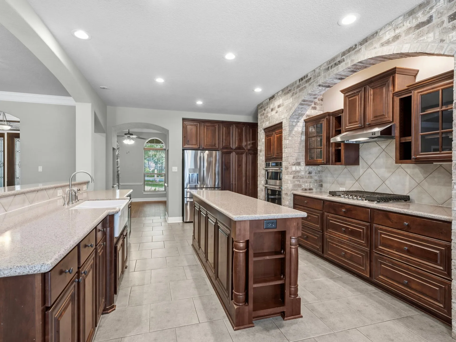 Vacant kitchen island with dark wood cabinetry, granite countertops, and brick arched accent wall
