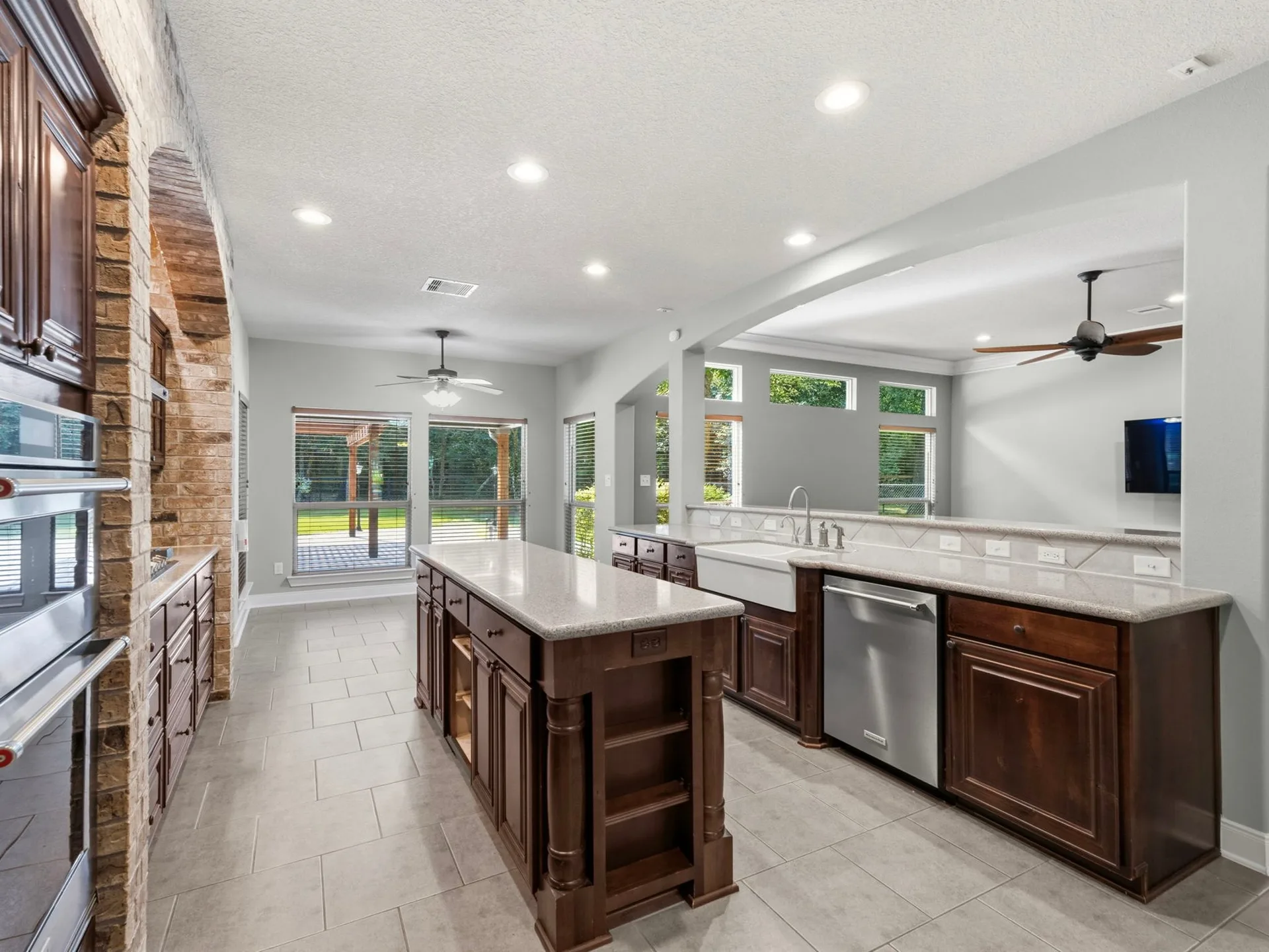 Wide-angle kitchen with dark wood cabinets, quartz countertops, brick arch, farmhouse sink, and stainless appliances