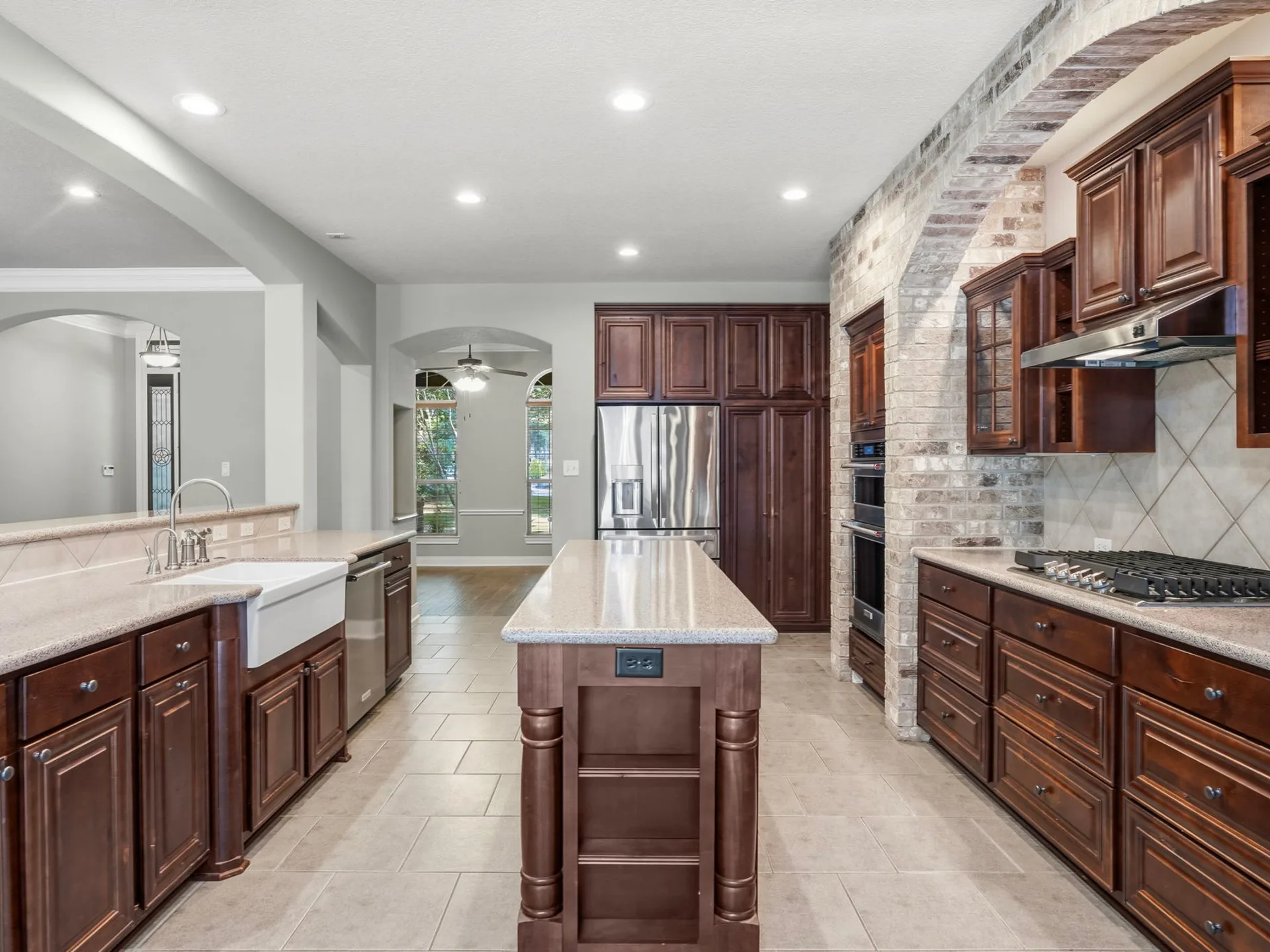 Wide-angle kitchen with large island, farmhouse sink, double ovens, and brick archway detail