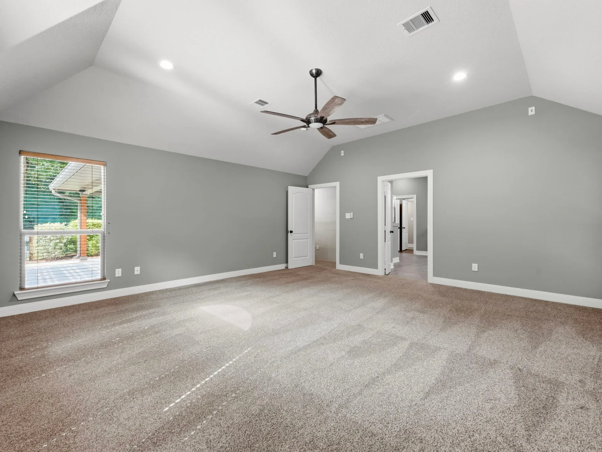 Master bedroom with vaulted ceiling, neutral gray walls, carpeted flooring, and single window with natural light