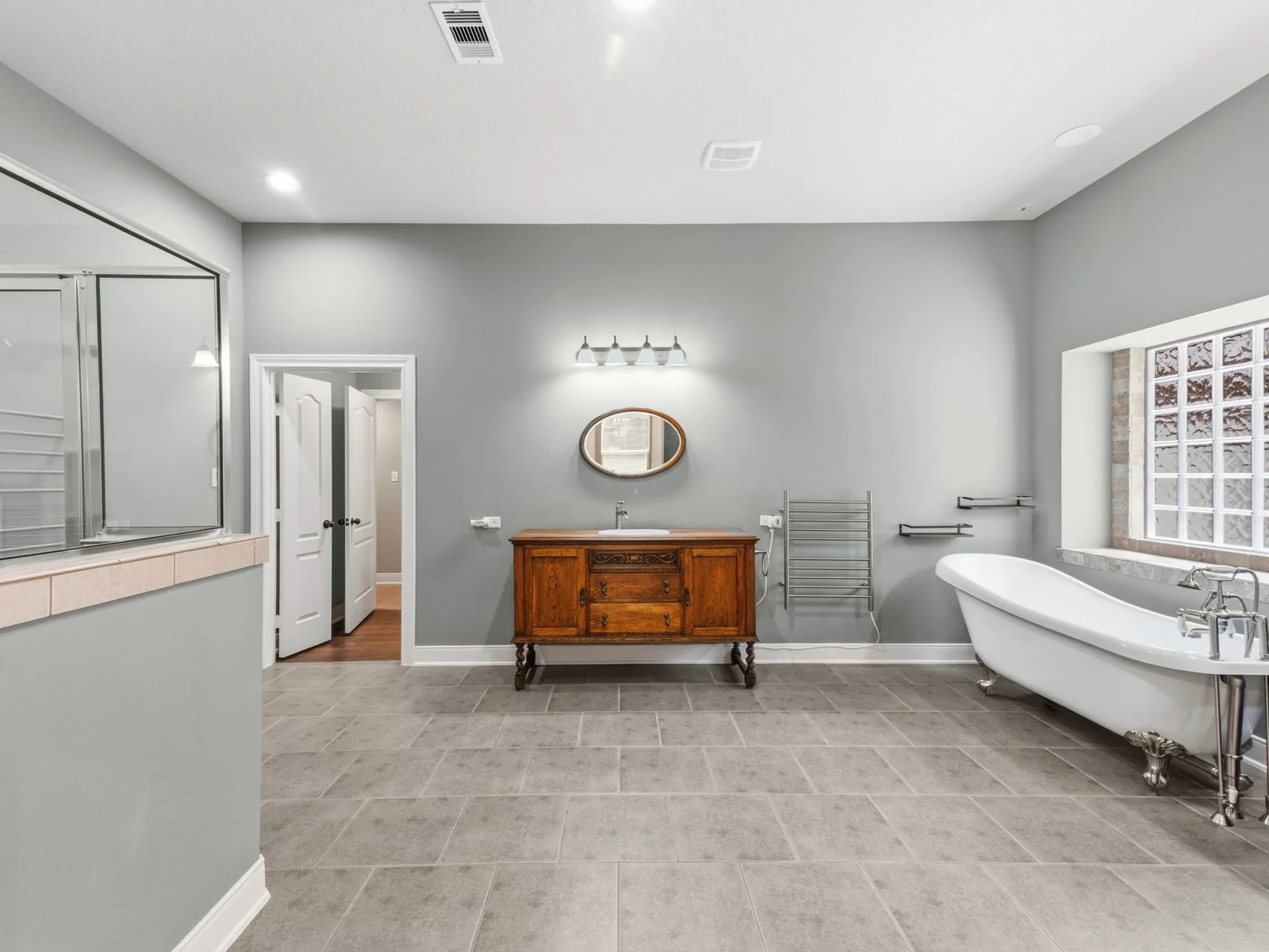 Primary bathroom with traditional wood vanity, oval mirror, clawfoot tub, and gray tile flooring