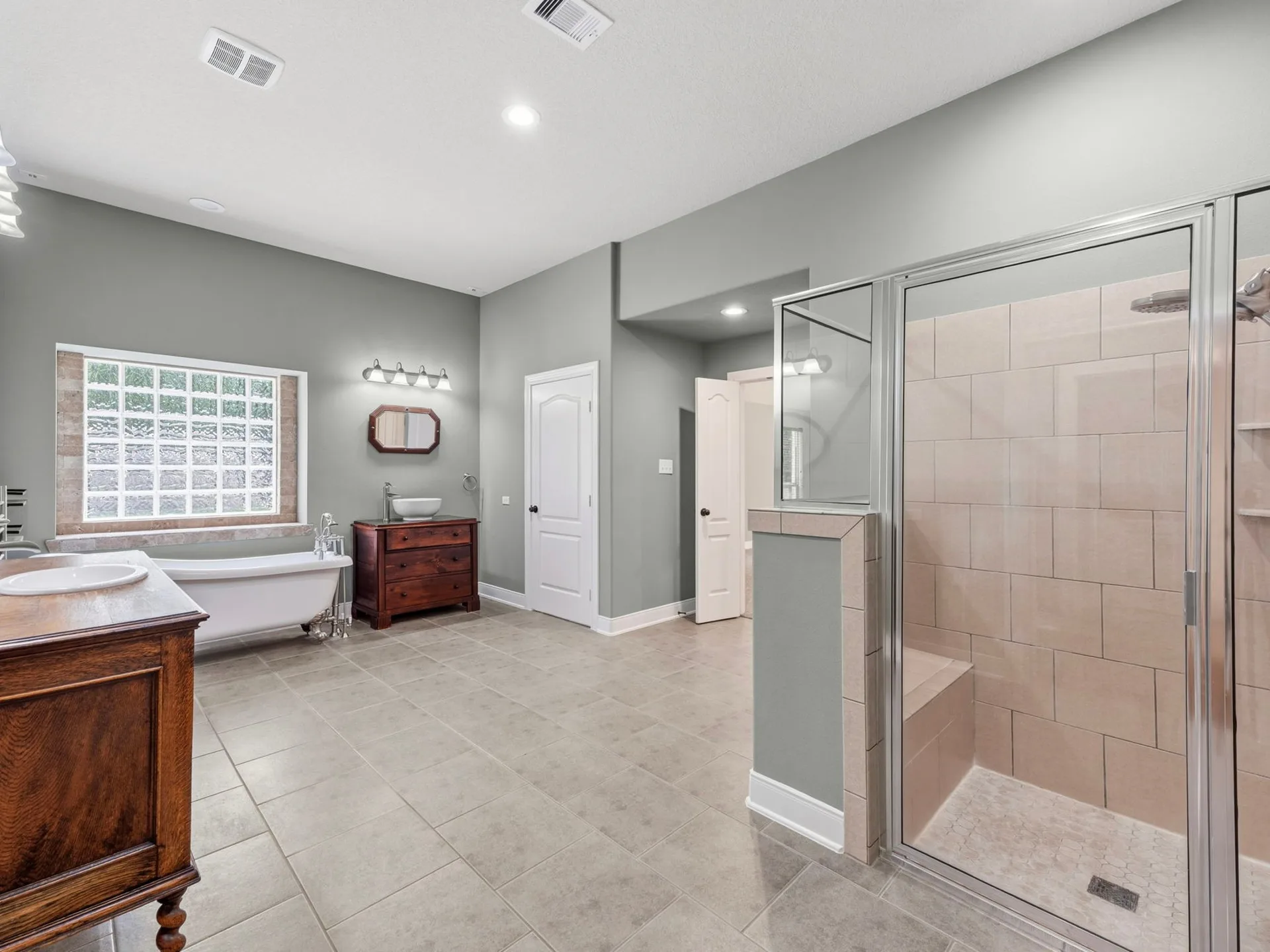 Wide-angle primary bathroom with double vanities, walk-in shower, glass block window, and clawfoot tub