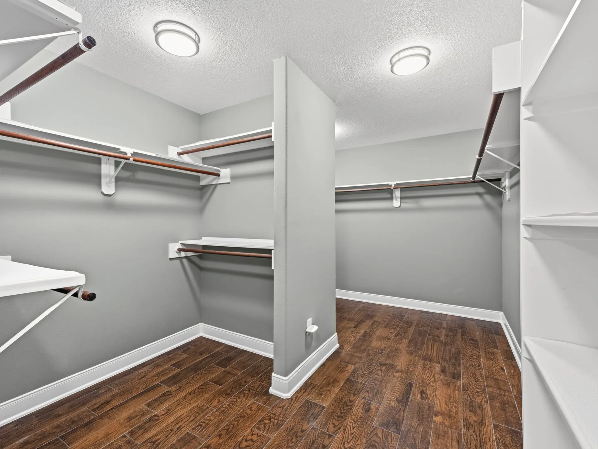Walk-in closet with neutral grey walls, wood-look plank flooring, and white shelving with hanging rods