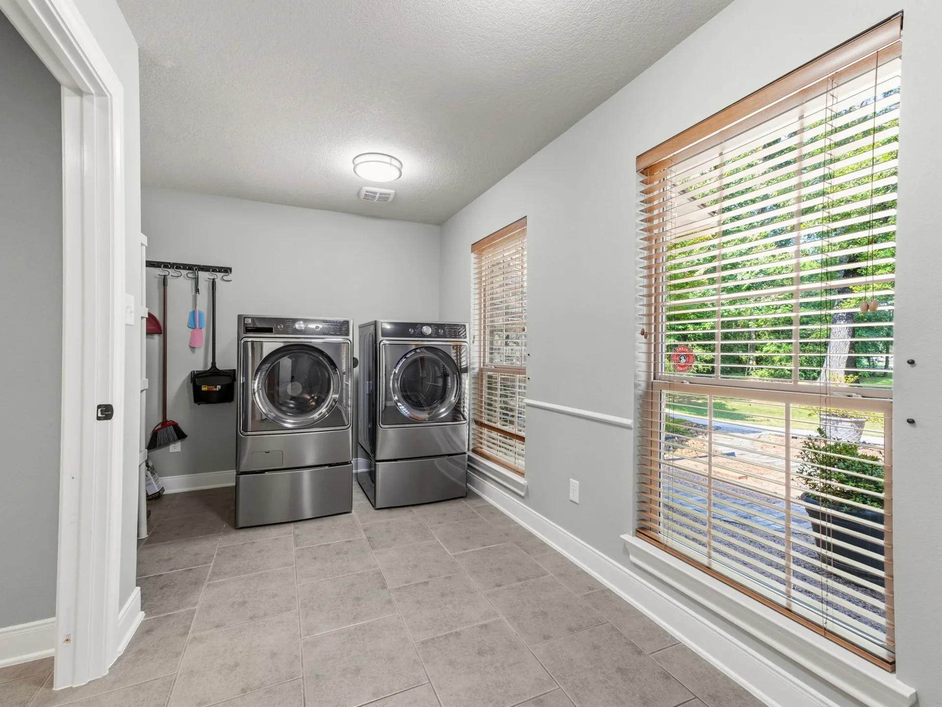 Laundry utility room with tile flooring, large windows, wood-tone blinds, and washer-dryer hookups