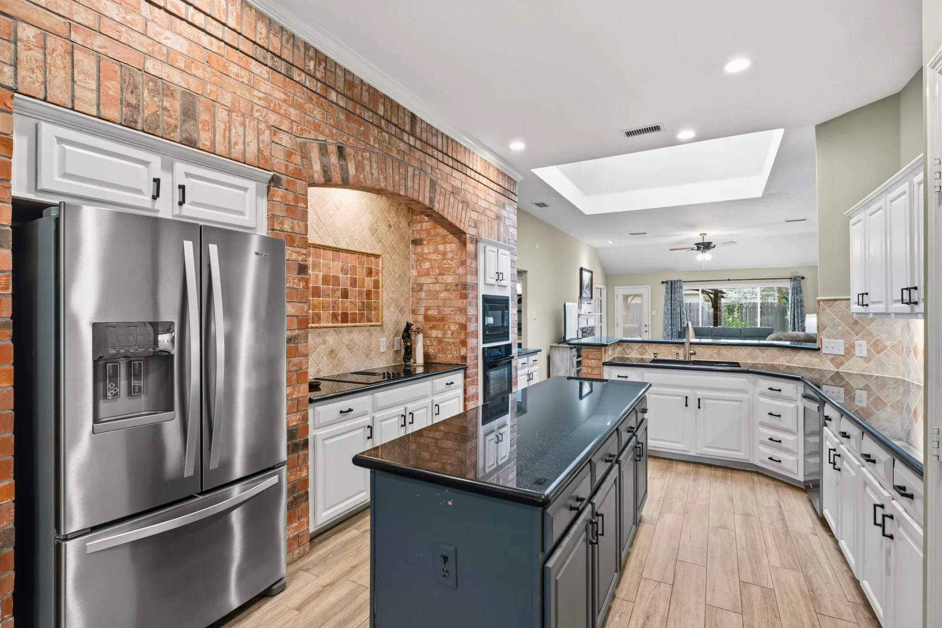 Updated kitchen with white cabinetry, island, and brick arch