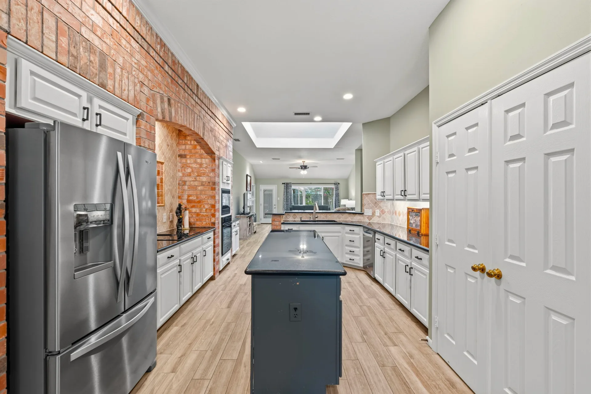 Kitchen open to family room with white cabinets, dark granite counters, and brick arch detail