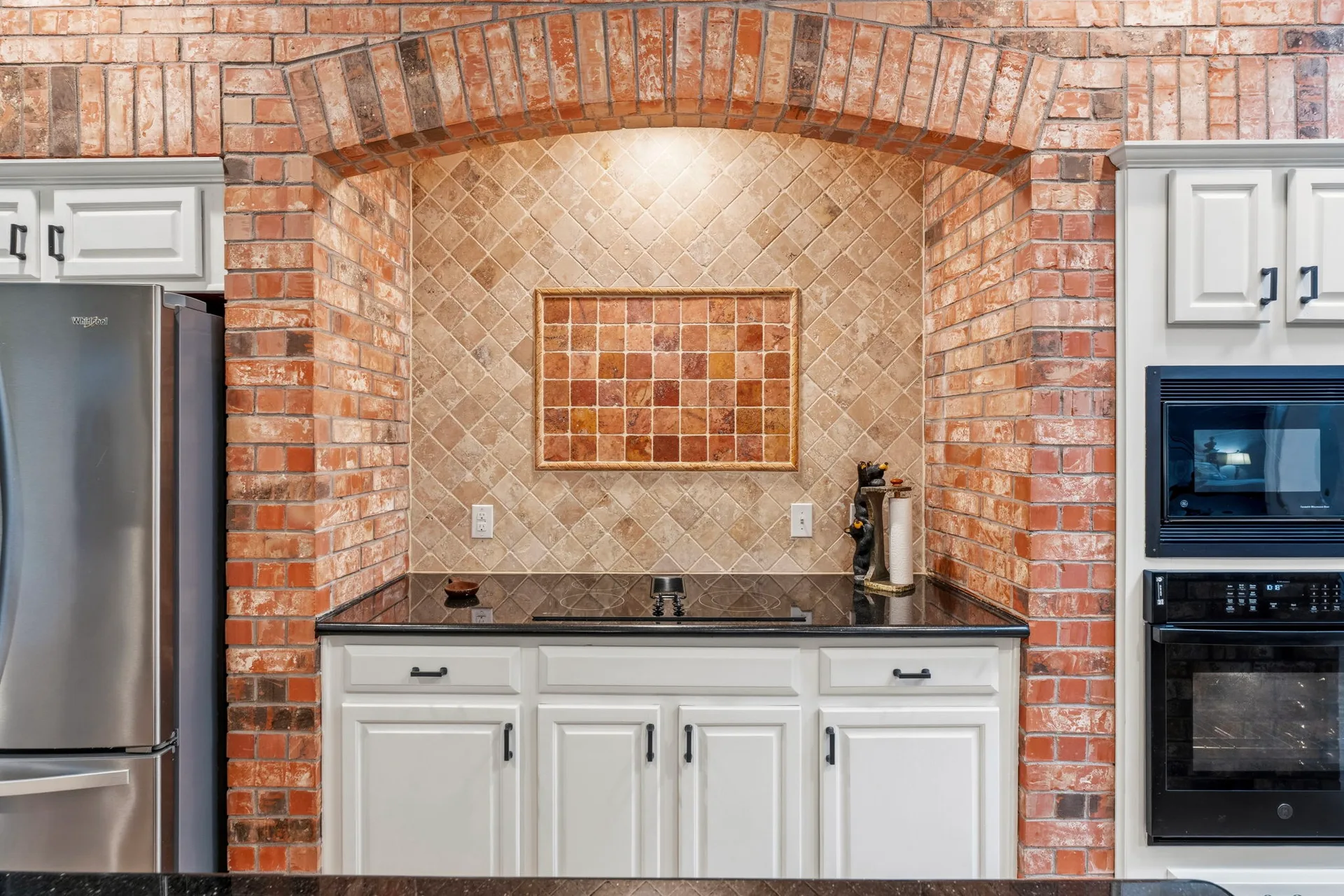Cooktop alcove with exposed brick arch and stainless steel appliances