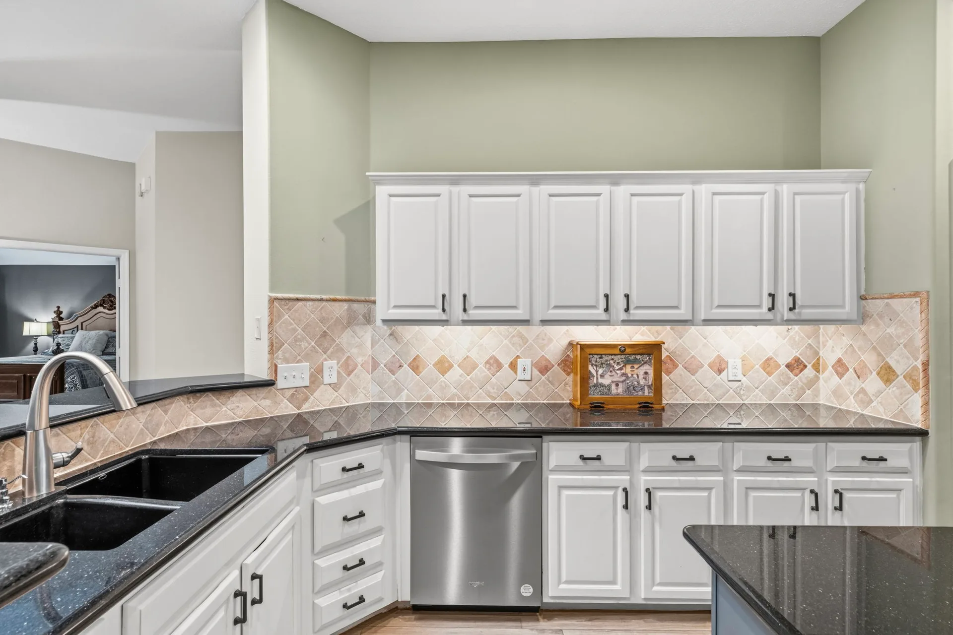 Kitchen sink area with white cabinetry, diamond-pattern backsplash, and granite counters