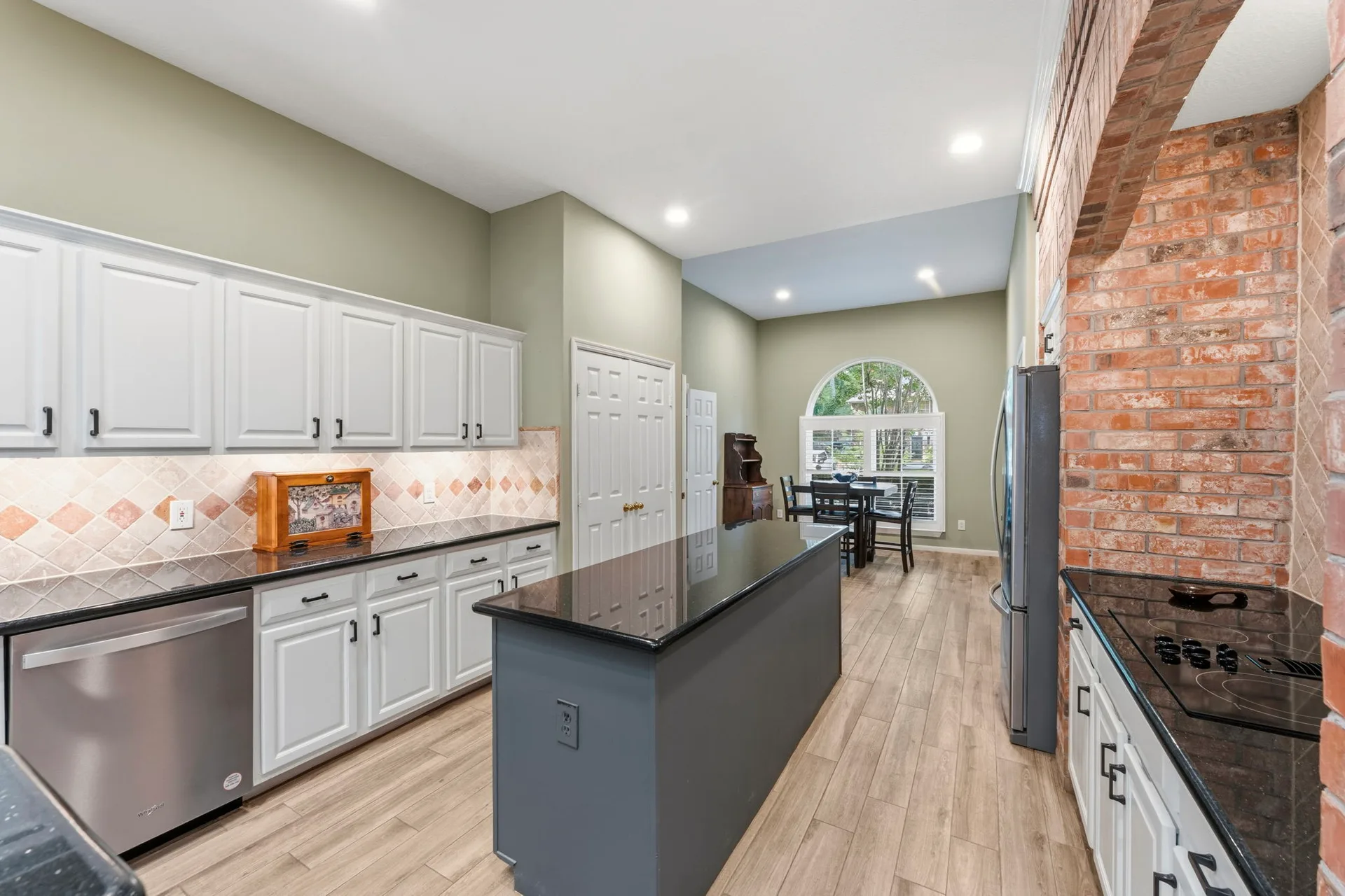 Wide kitchen shot showing island, brick arch, and open connection to dining area