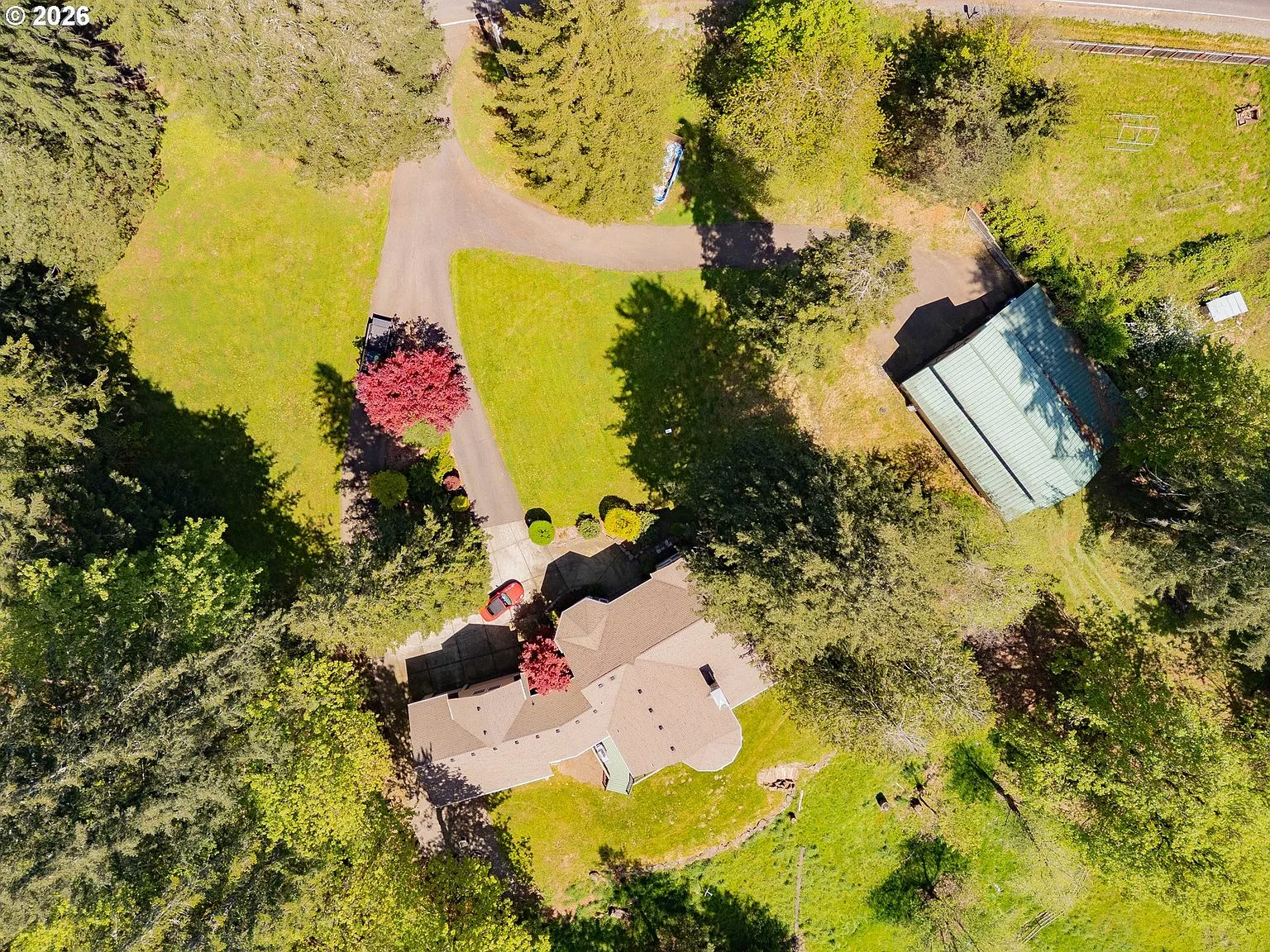 Aerial view of the full parcel: house, barn, split driveway, and wooded acreage
