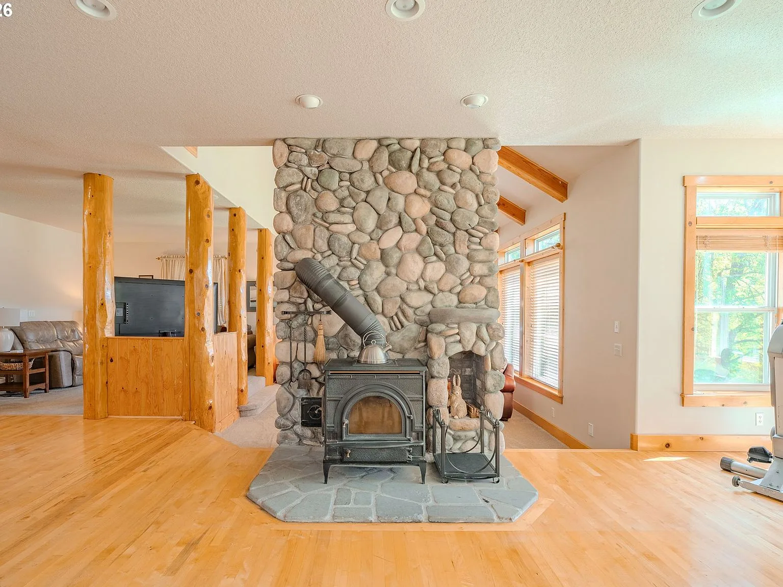 Great room with river rock fireplace, wood stove, and vaulted beamed ceiling