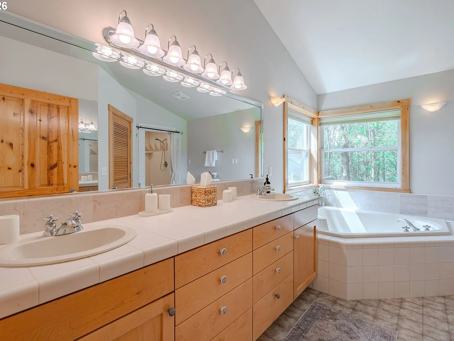Master bathroom with light wood vanity, tiled countertop, and natural daylight
