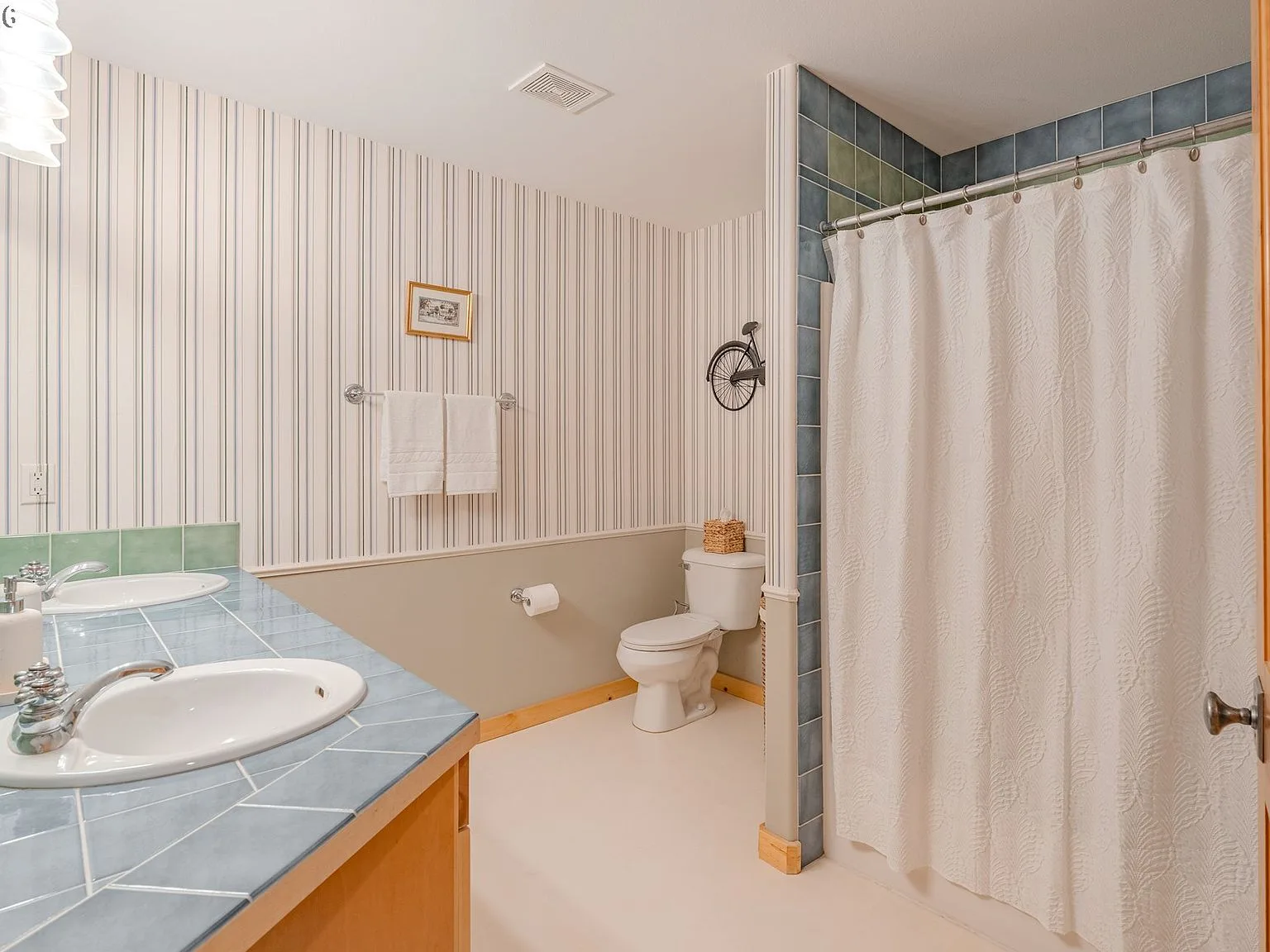 Bathroom with double vanity, striped wallpaper, and blue tile countertop