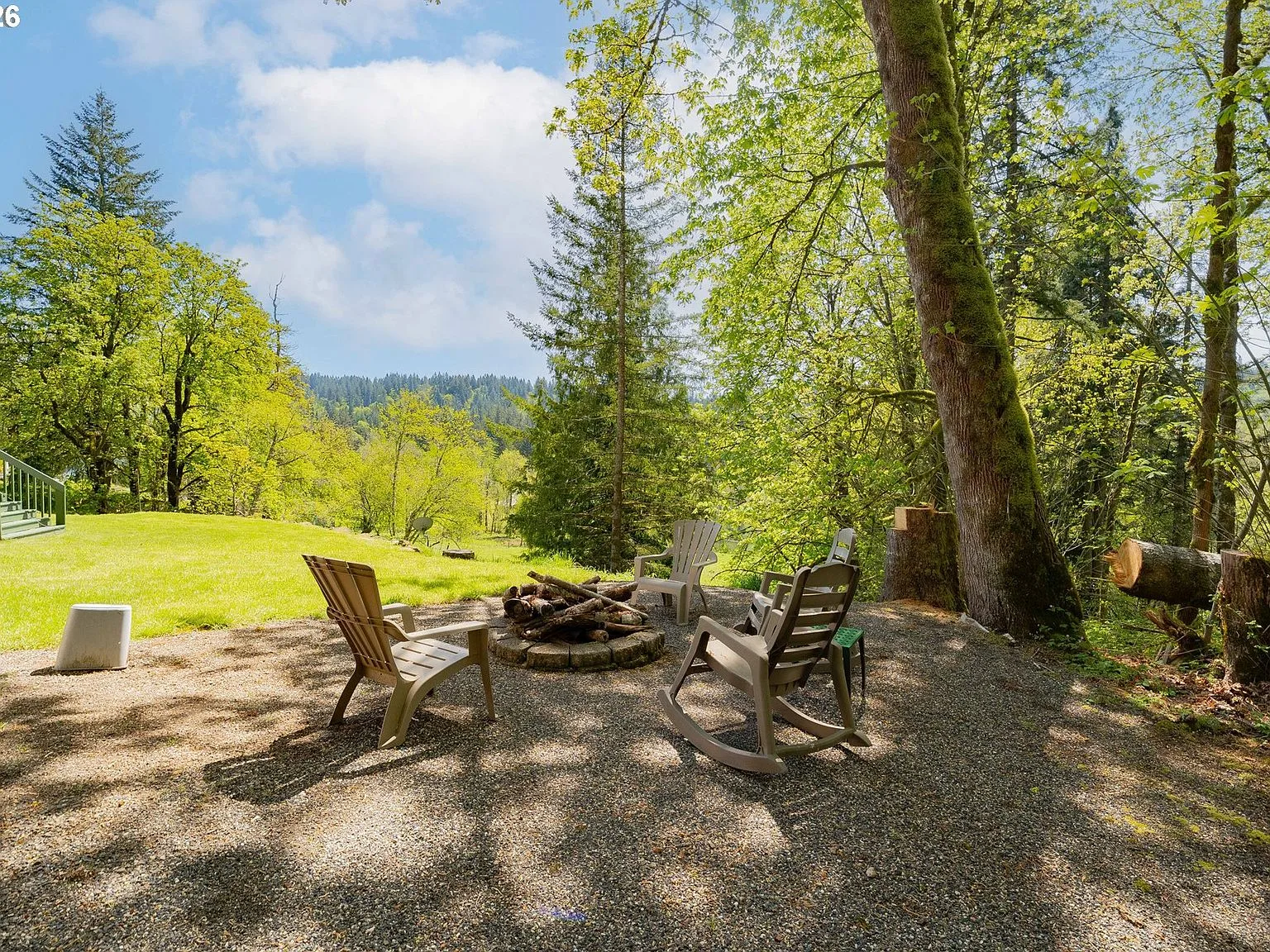 The fire pit under mature maples and firs, chairs gathered around