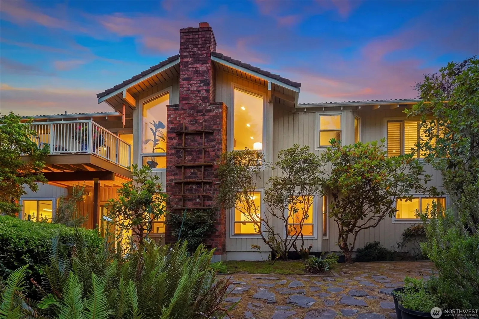 Rear facade of a two-story Bellevue home with a prominent brick chimney and raised wood deck at golden hour