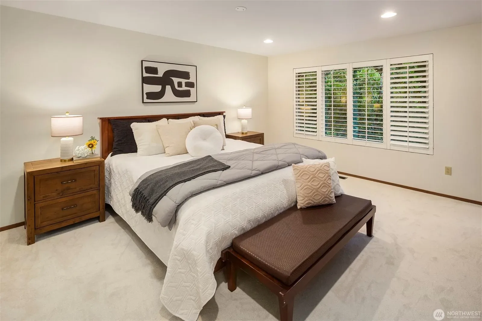 Primary bedroom with neutral tones, soft carpet, and a large window with shutters letting in gentle daylight