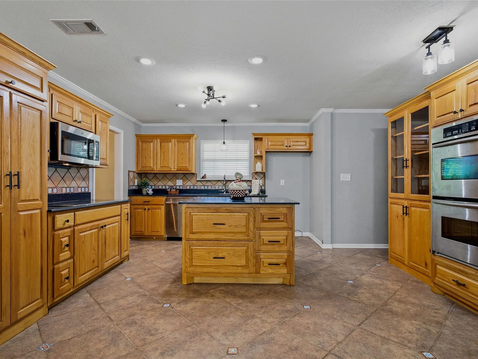 Kitchen with oak cabinetry, black countertops, island, and stainless steel appliances