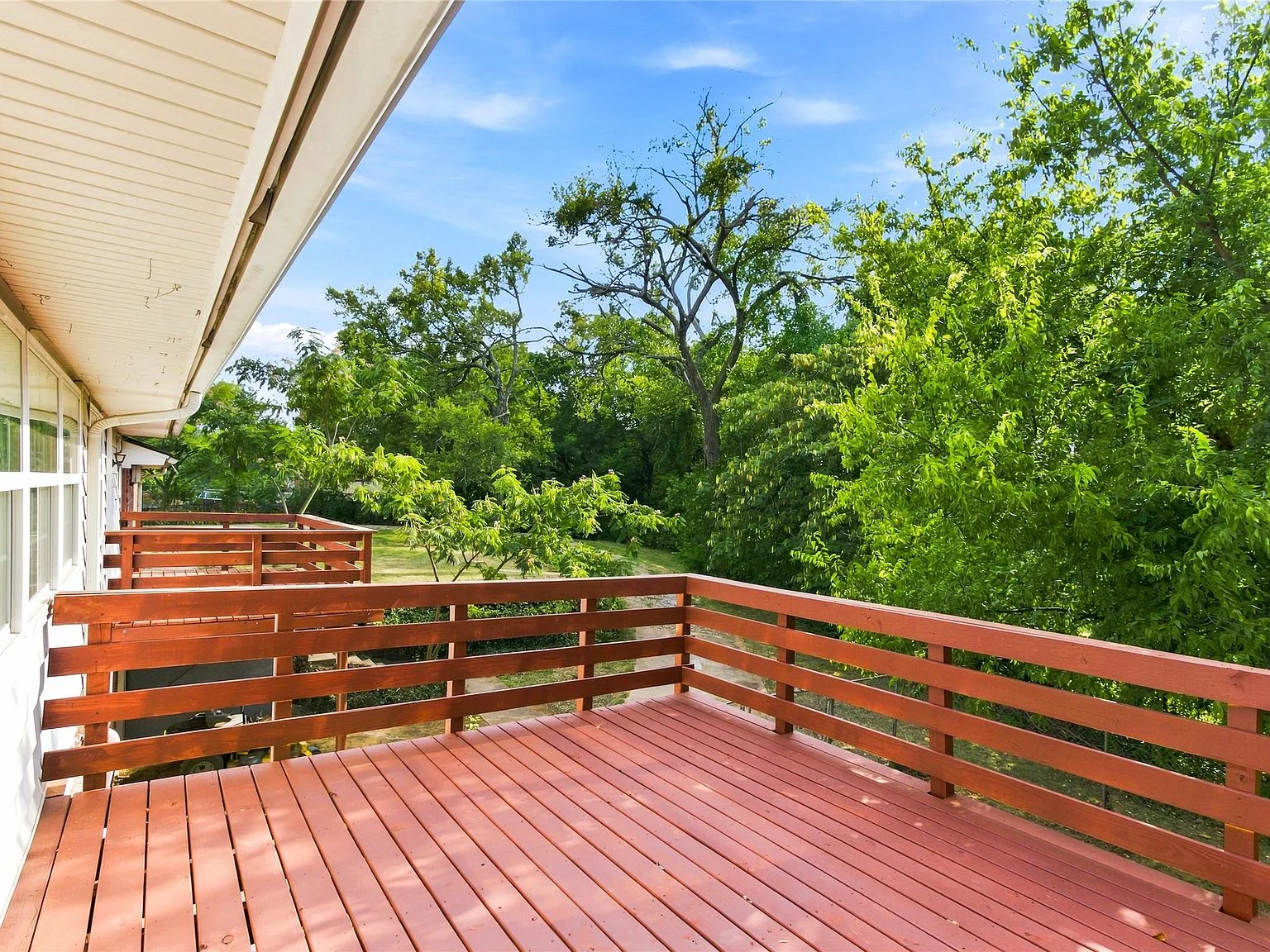 Wooden back deck overlooking mature trees with clear blue sky