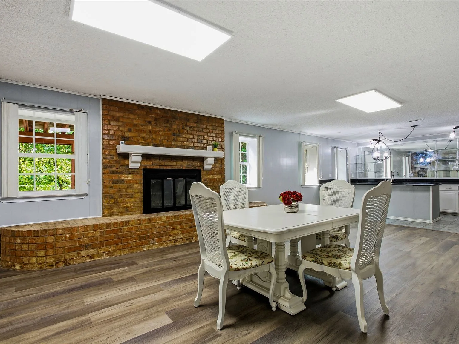 Basement dining room with exposed brick fireplace, white mantel, and plank flooring