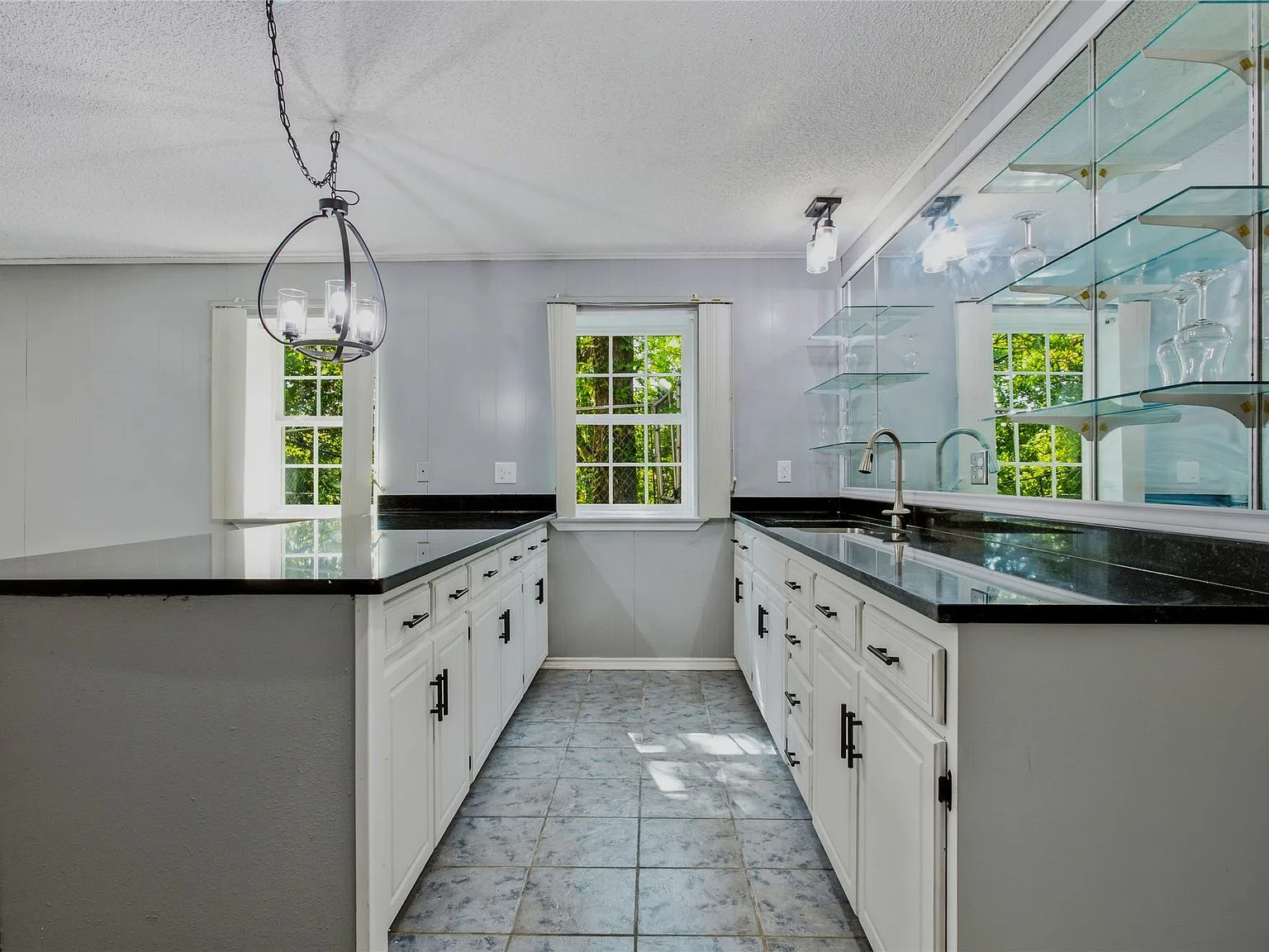 Updated kitchen with white cabinetry, black stone countertops, and glass display shelving