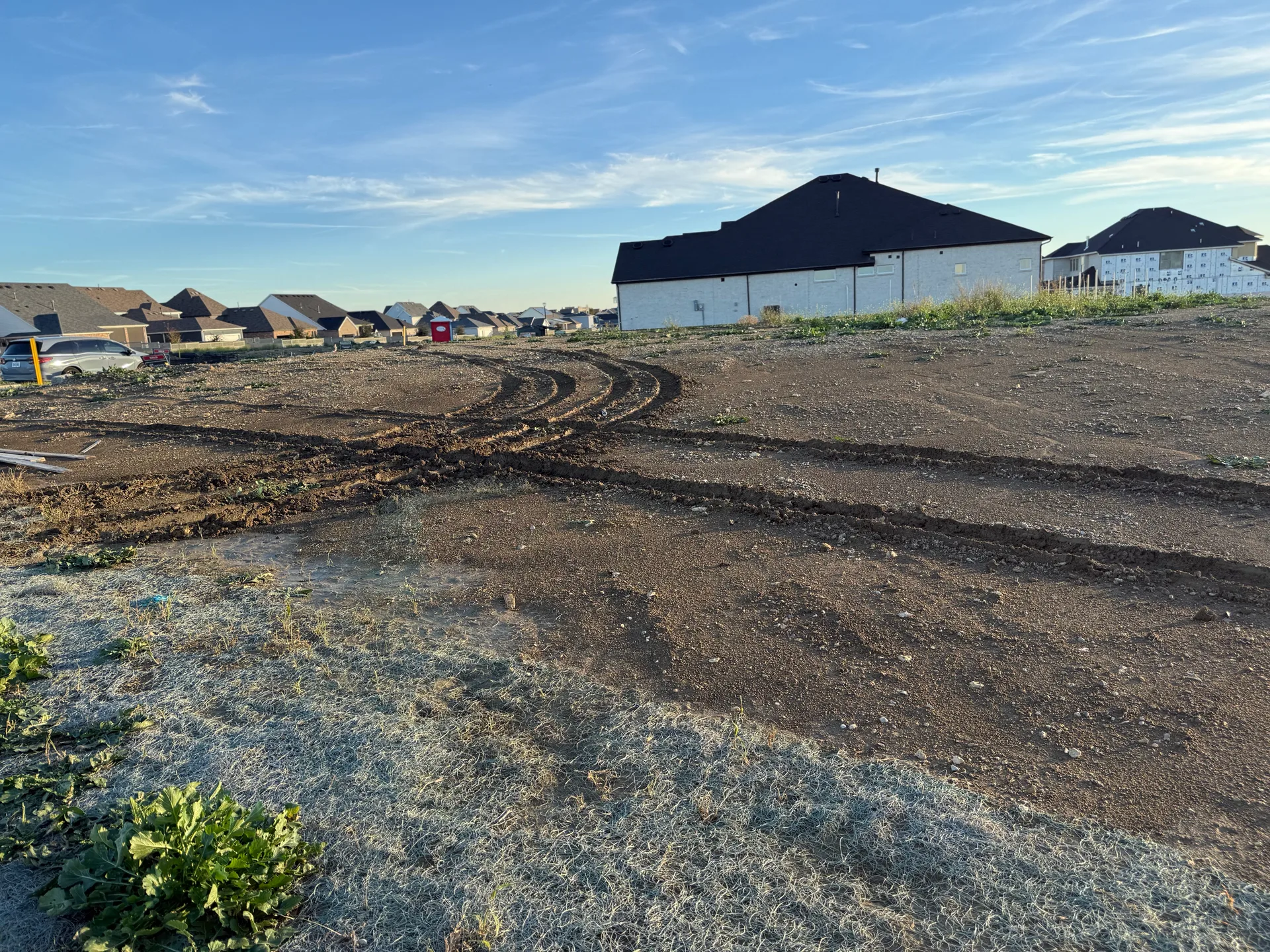 A cleared residential homesite under development in a North Texas new-construction community, with new homes in the background