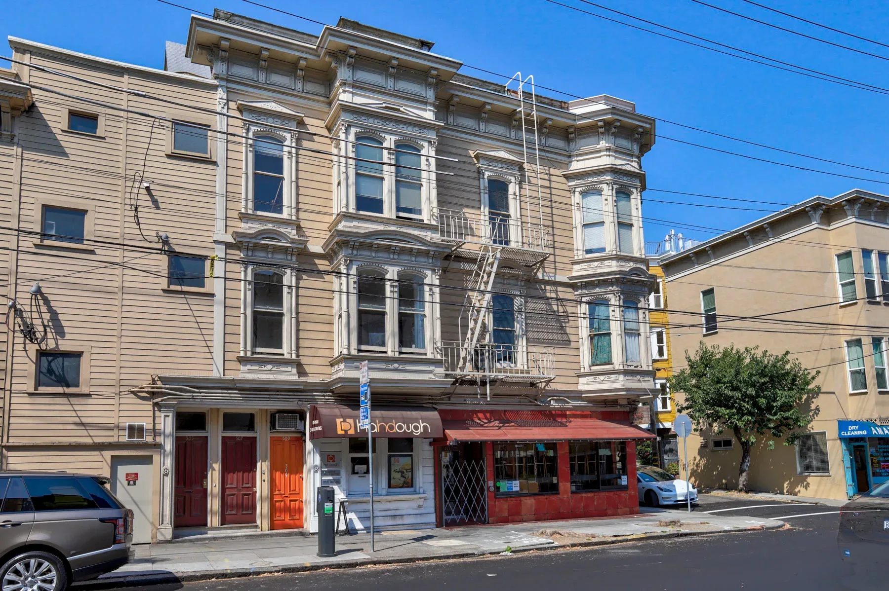 Victorian mixed-use building with tan wood siding and ground-floor storefronts