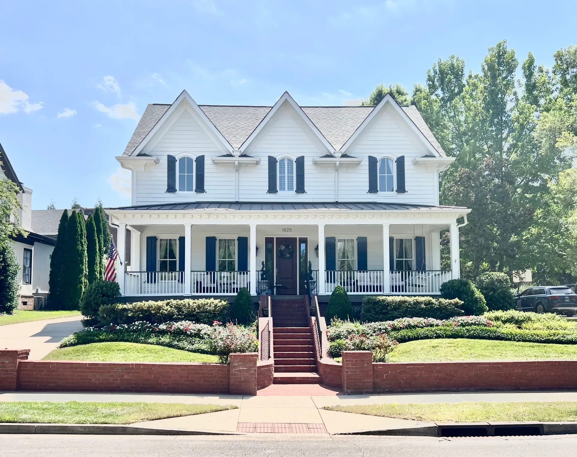 White farmhouse-style home in Westhaven, Franklin TN with black shutters, full front porch, and brick retaining wall