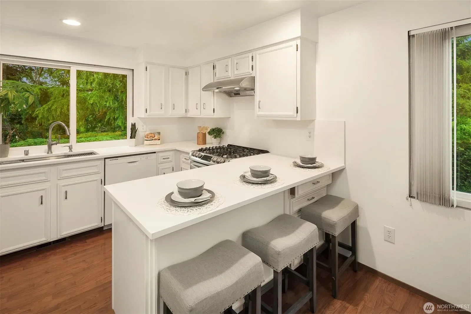 Updated kitchen with white cabinets, white countertops, peninsula with bar seating, and stainless steel appliances