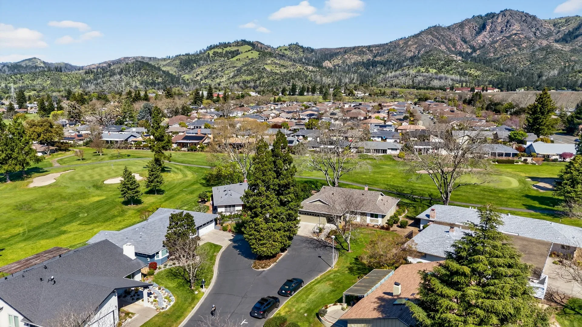 Aerial drone view of Oakmont Village residential neighborhood bordering the East Course, with golf course fairways and Hood Mountain views in the distance