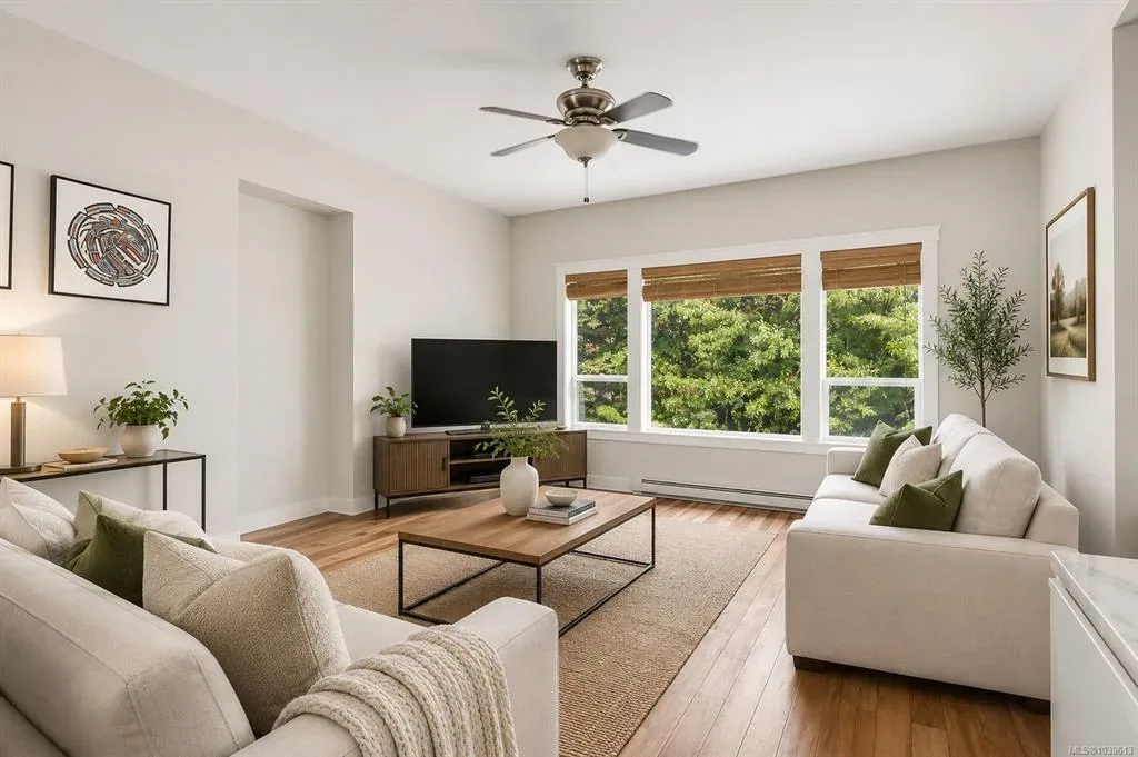Main-floor living area with neutral sofas, wood flooring, and natural light through large windows