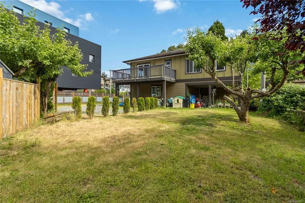 Generous fenced backyard with mature trees, lawn, and raised wooden deck