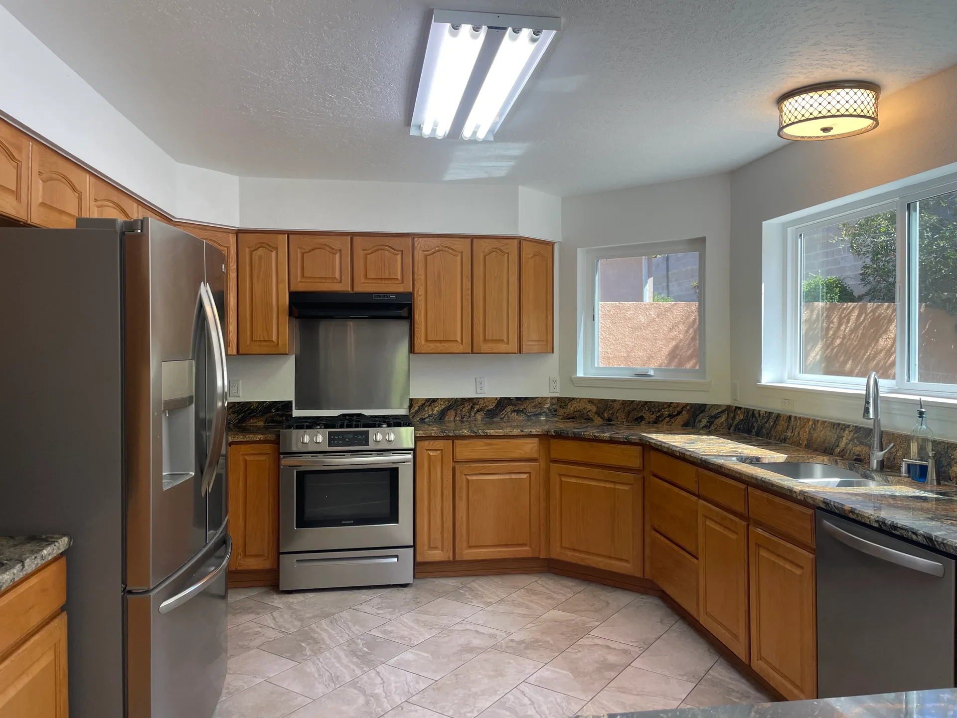 Wide view of the kitchen with natural wood cabinetry and patterned granite countertops