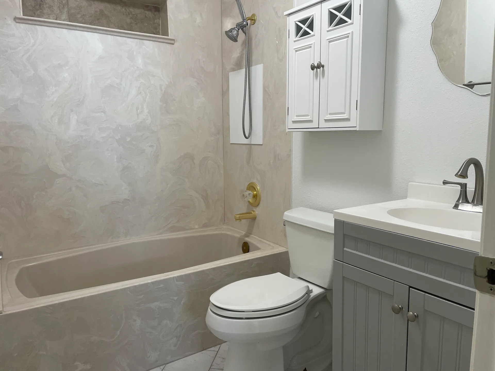Bathroom with grey vanity cabinet, white countertop, and beige marble-look tub surround