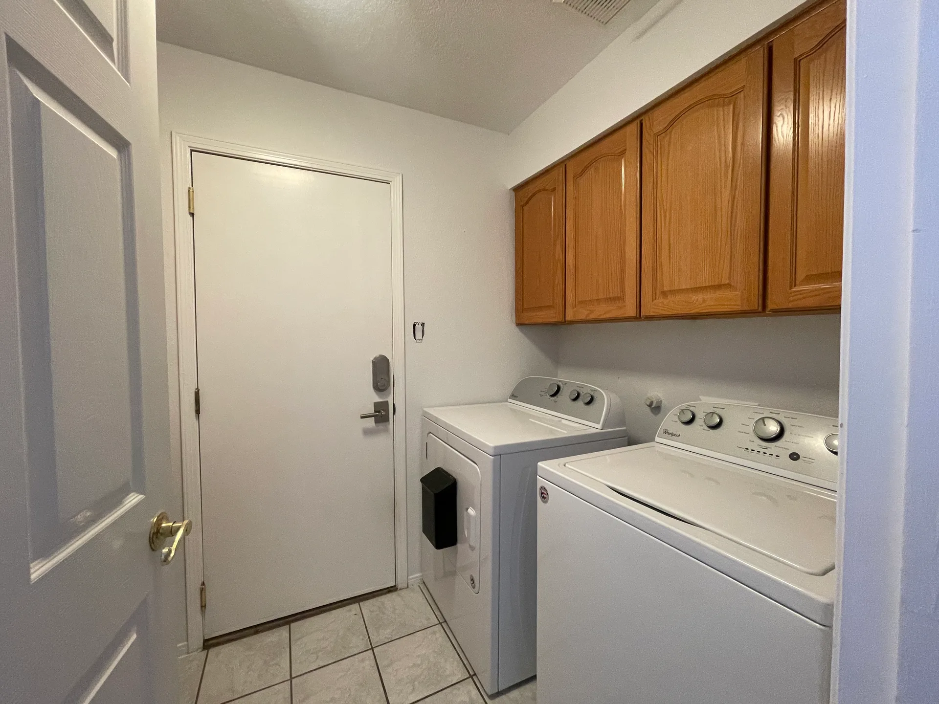 Laundry room with tile flooring and wood-finish upper cabinets