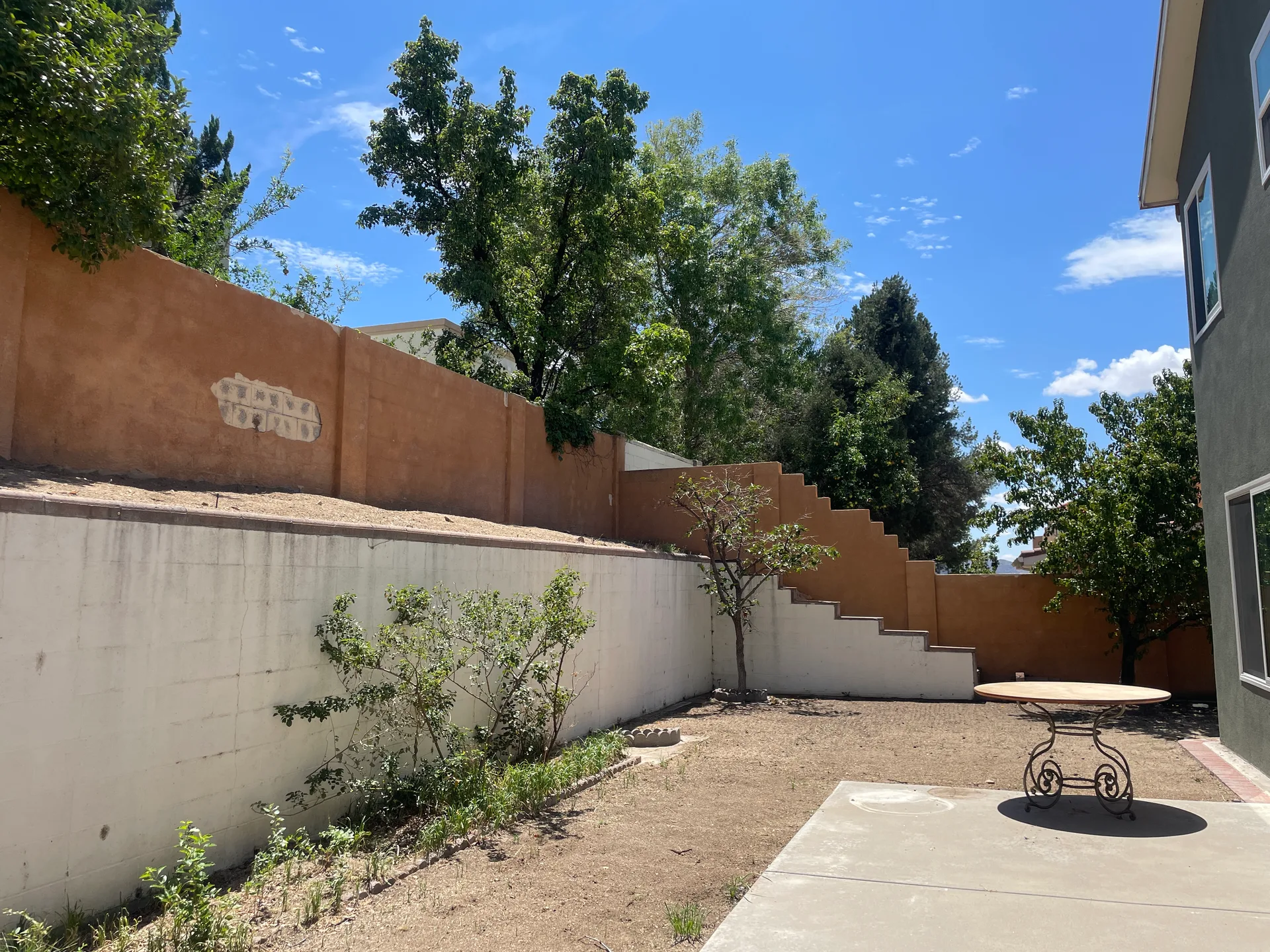 Backyard with tiered stucco retaining walls and a concrete patio under blue sky