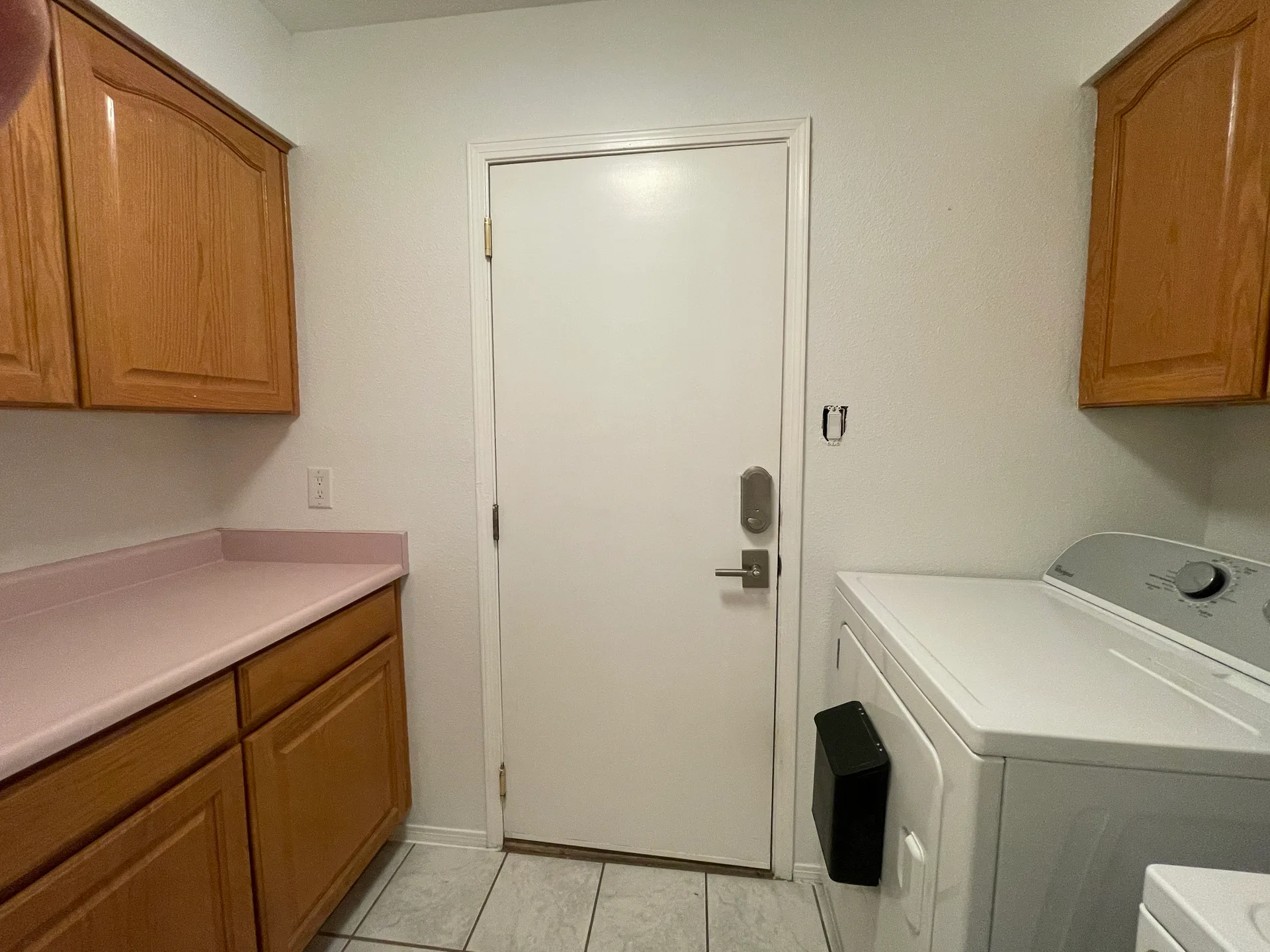 Laundry room with honey-oak cabinets, pink laminate countertops, and a white door