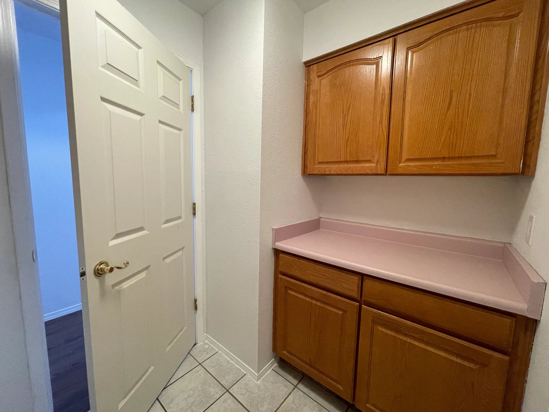 Vacant laundry utility room with medium-tone wood cabinetry and white tile flooring