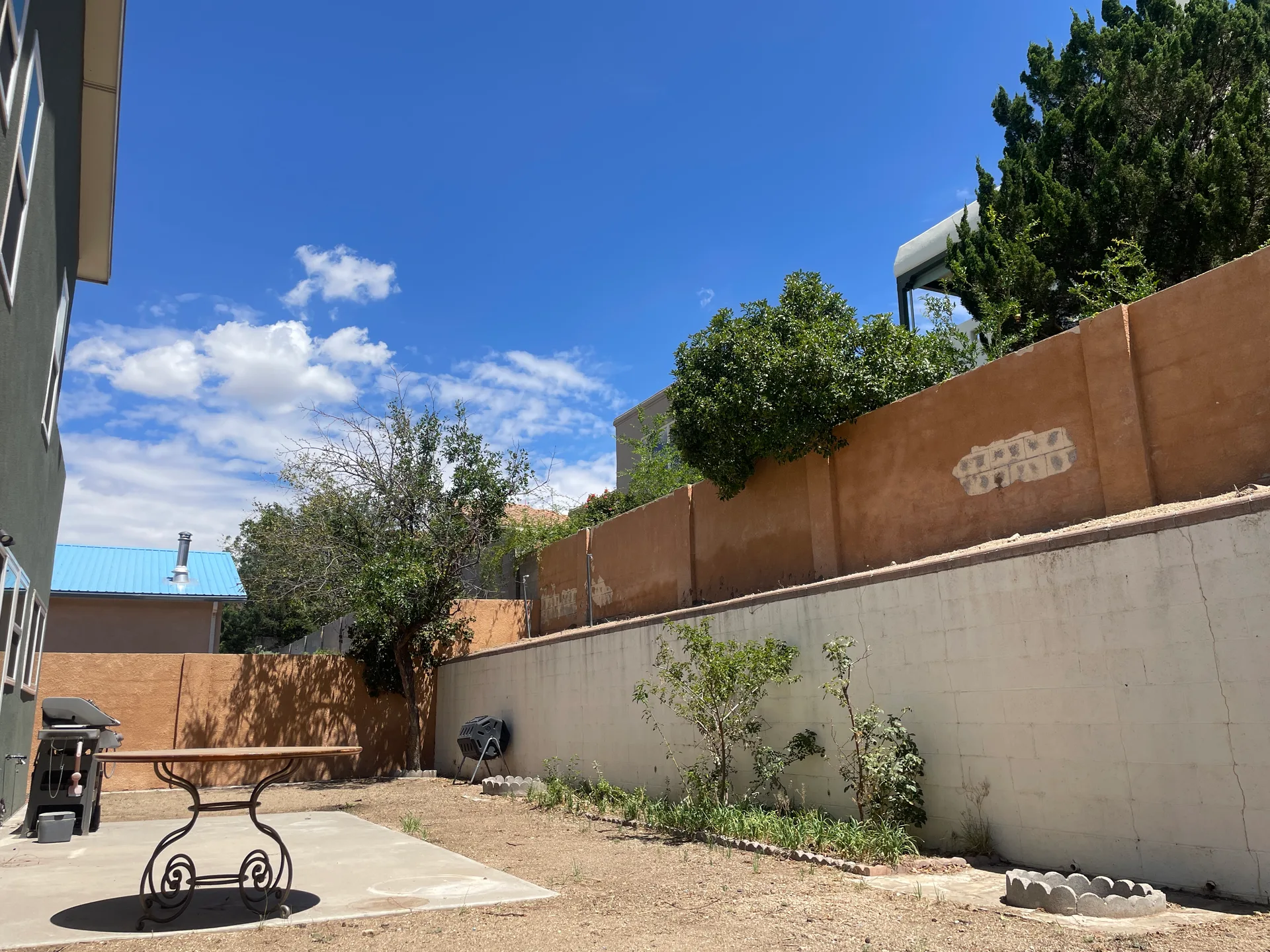 Backyard with concrete patio, perimeter stucco wall patches, and clear blue sky