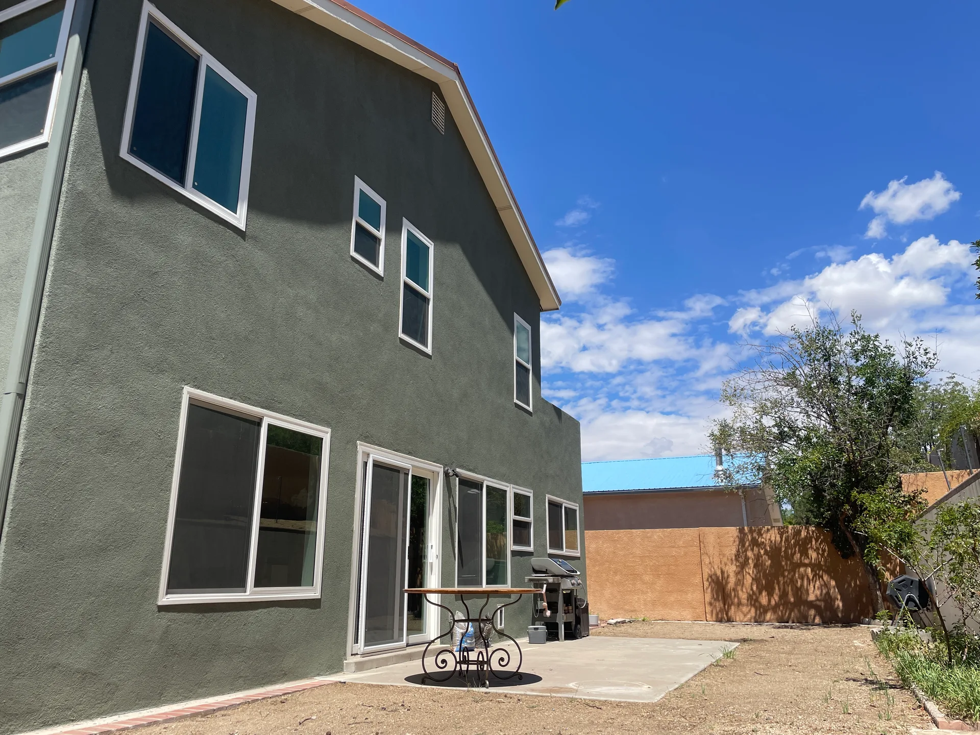 1506 Wells Dr NE rear exterior with two-story grey stucco facade, patio, and blue sky