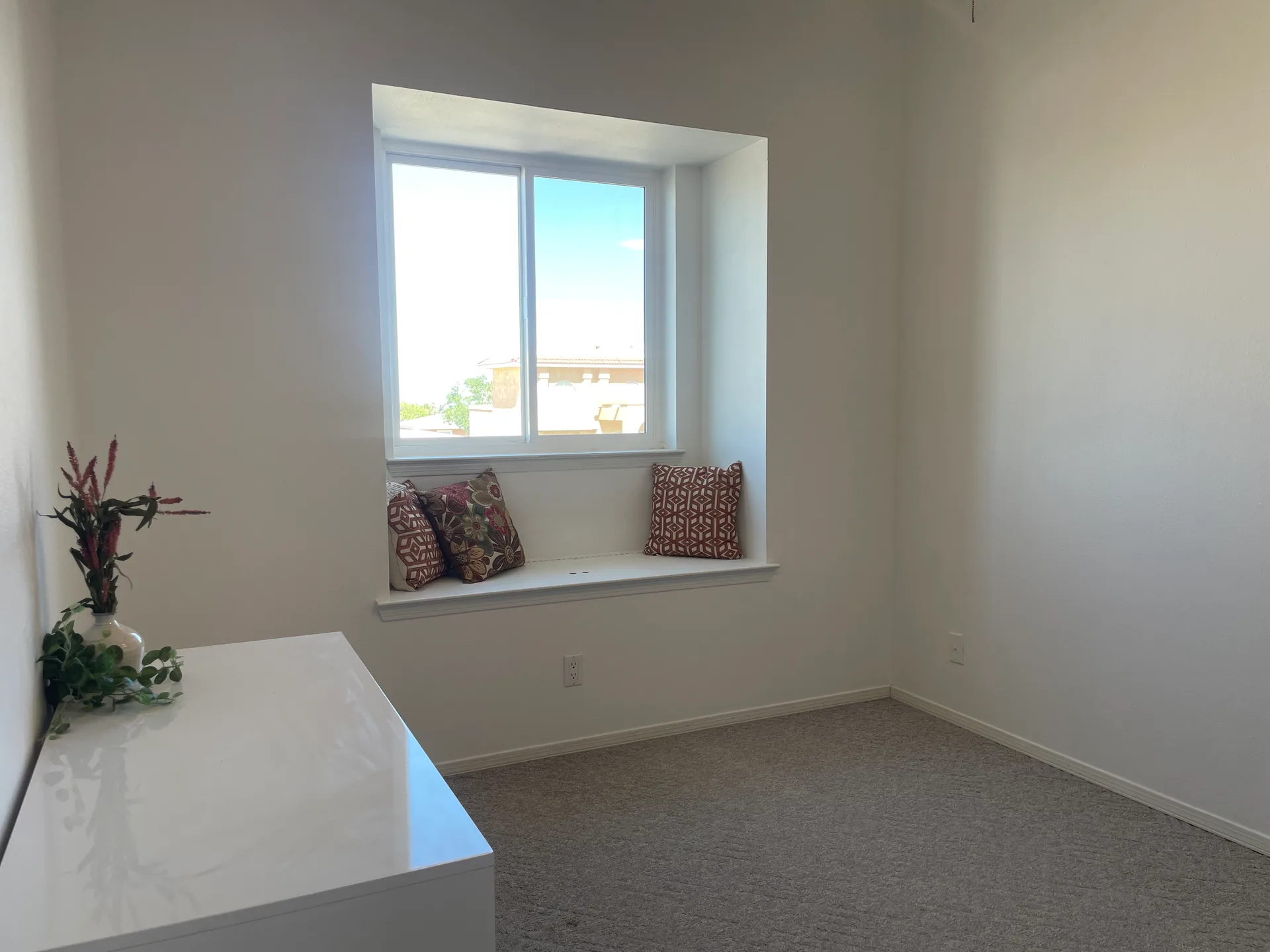 Bright bedroom with window seat, white walls, and neutral carpet