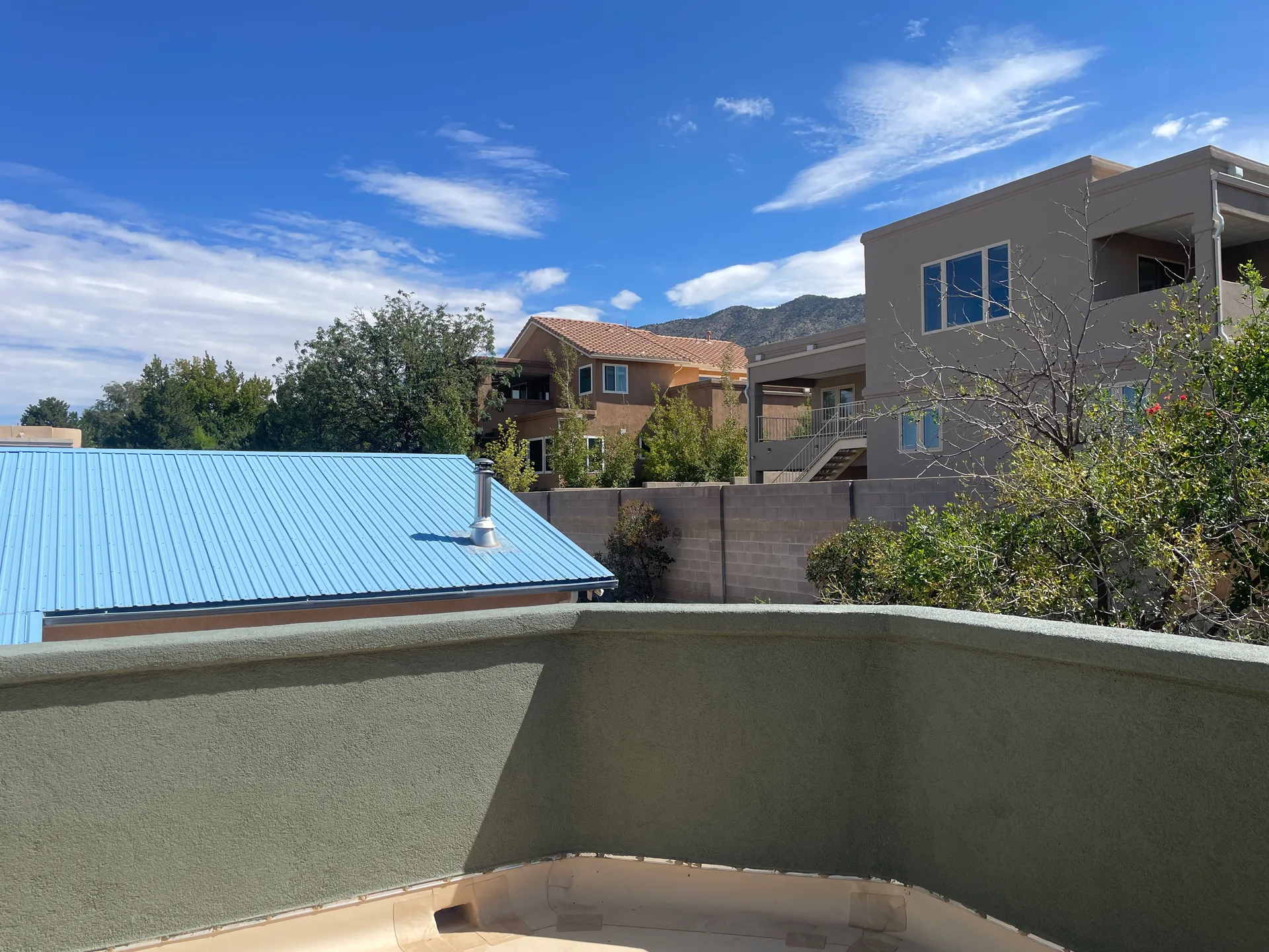 Balcony view with stucco wall, metal roof, and desert landscape background under blue sky