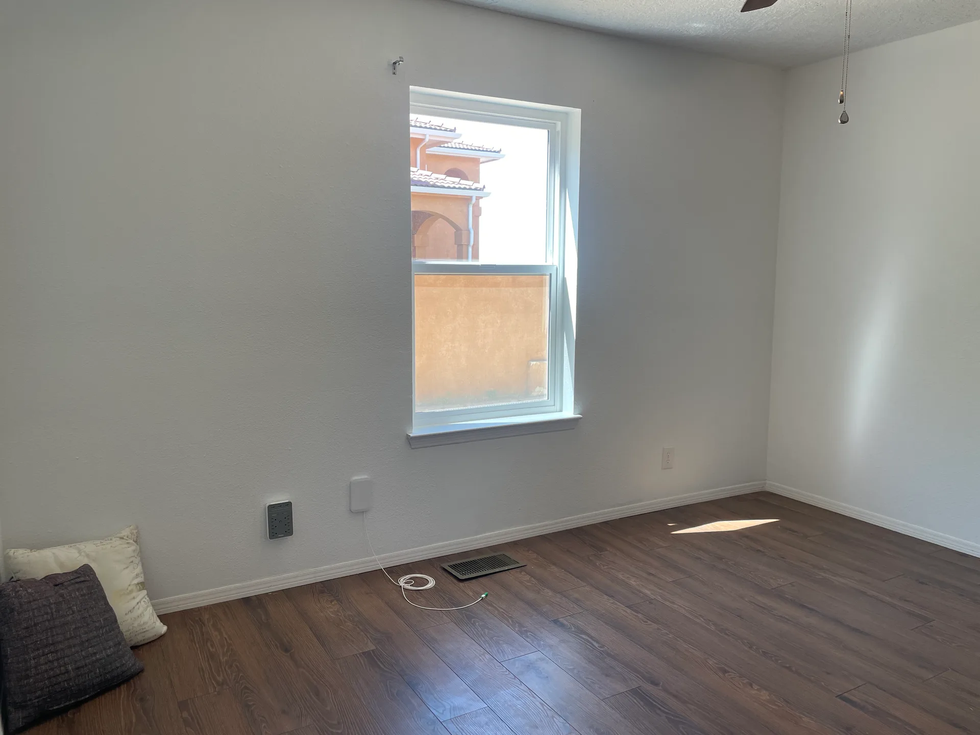 Vacant bedroom with white walls, dark wood-look laminate flooring, and a window