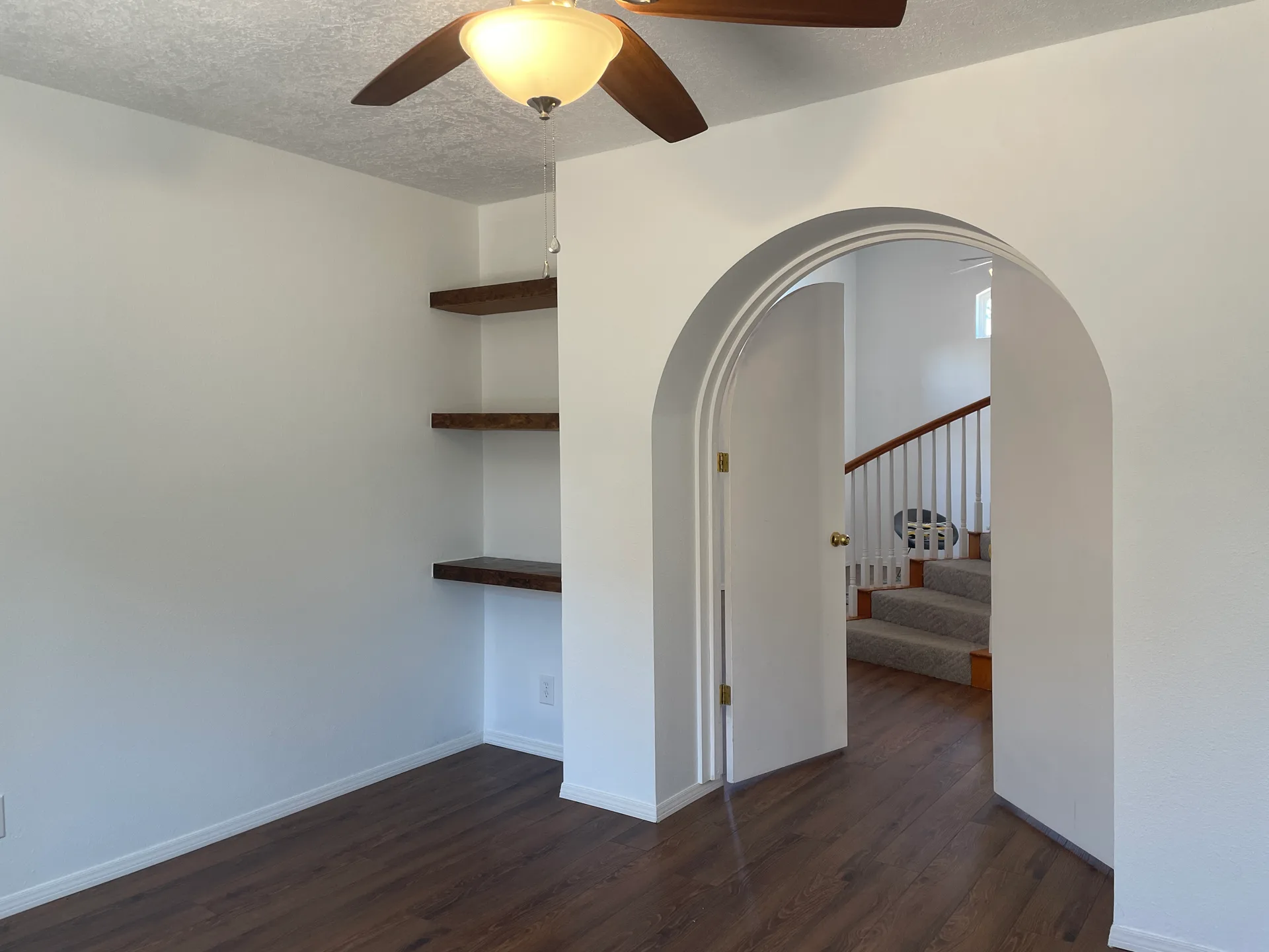 Bedroom with arched doorway leading to stairs, white walls, and wood-tone flooring
